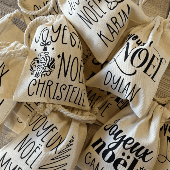 Gros plan sur des pochons en coton personnalisés avec inscriptions Joyeux Noël et prénoms, pour offr