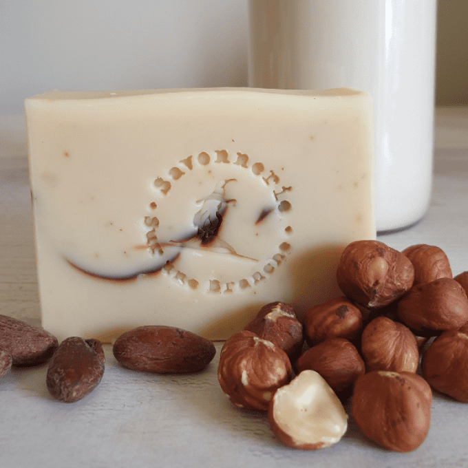 Savon surgras au lait de noisette avec noisettes entières en décor et pot de lait en arrière-plan