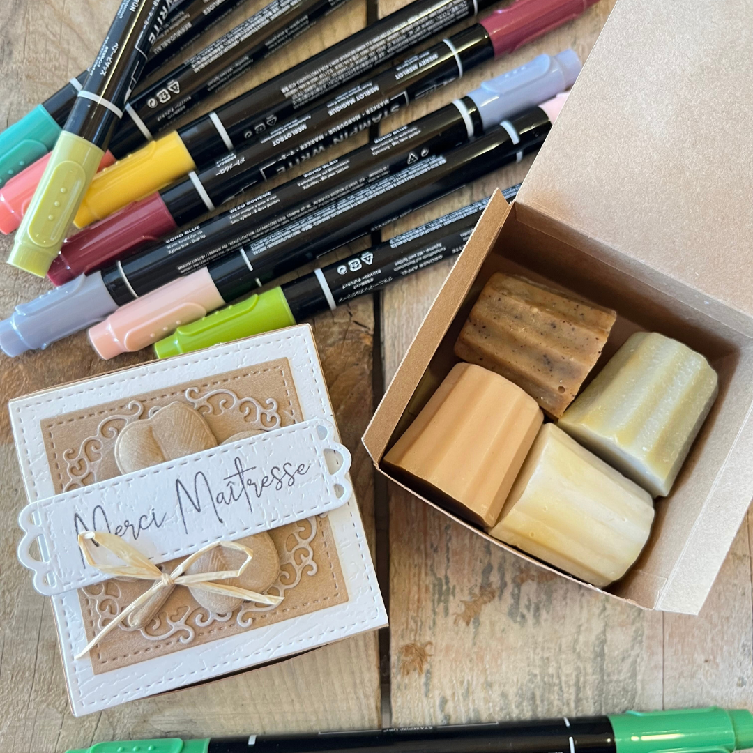 Boîte cadeau contenant quatre savons artisanaux en forme de cannelés, avec étiquette "Merci maîtresse" et décoration naturelle.
